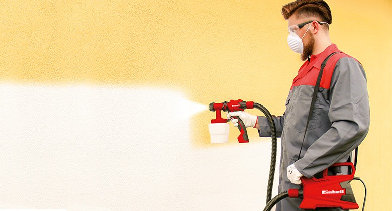 man using a paint spray gun to colour a wall